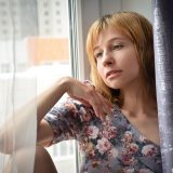 午后窗边一位审校人员手持红笔核对妹居物语稿件，阳光斜照在纸页上